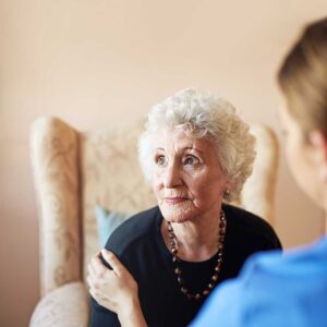 Older adult and caregiver having a calm conversation in a bright assisted living common room.